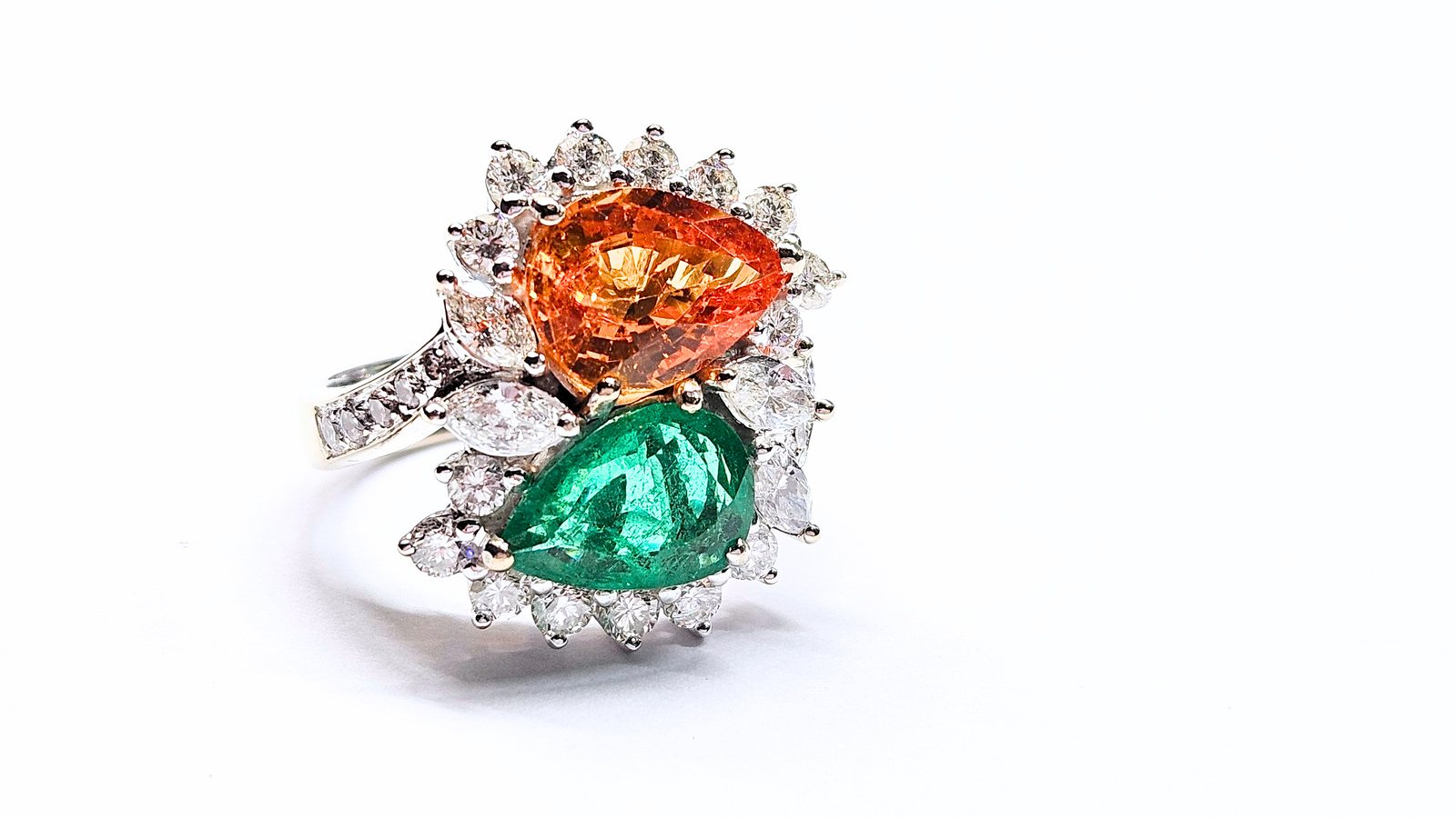A white gold ring set with a pear cut orange garnet and a pear cut emerald, framed with diamonds