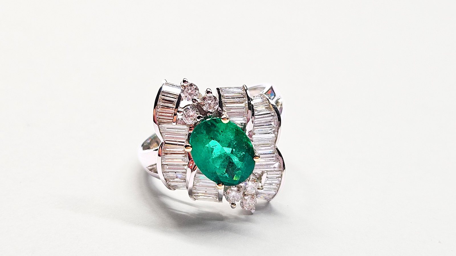 An oval emerald in a white gold cocktail ring with baguette and brilliant cut diamonds