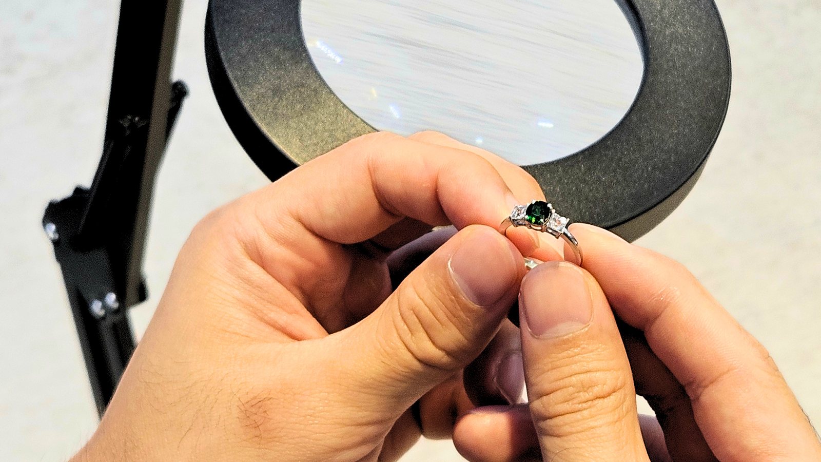A jeweller examining a green gemstone ring under a bench magnifier