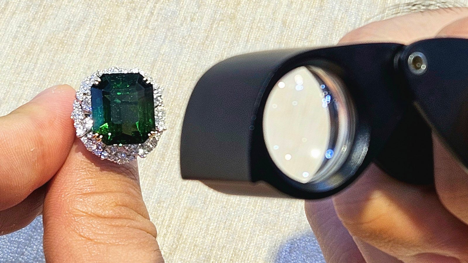 A green gemstone ring held up beside a jeweller's loupe for examination